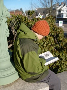 Ben reading a book in front of the decorative lamp with a lion's face in front of the Attleboro Public Library