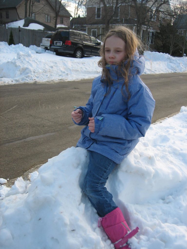 K pretending to ride a pony while sitting on a snow bank