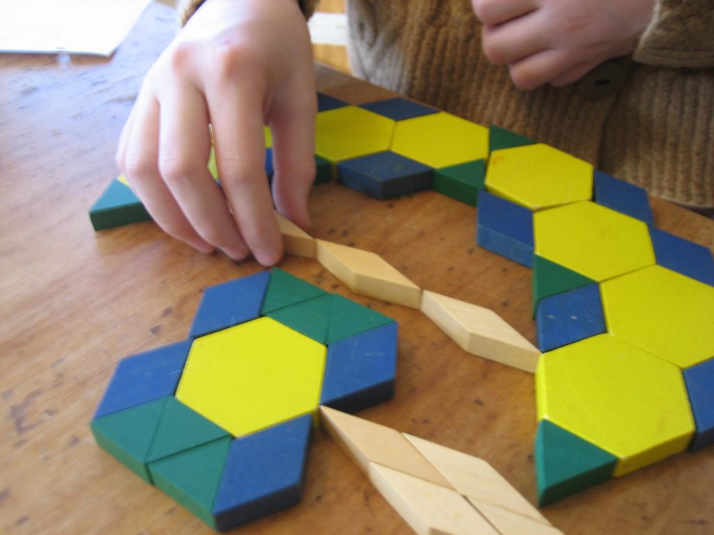 K's hand making a bow out of pattern blocks