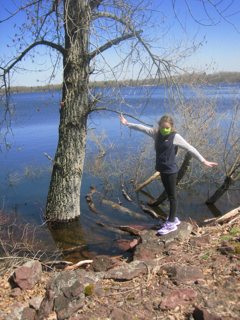 k balancing on rock by reservoir wearing a green facemask
