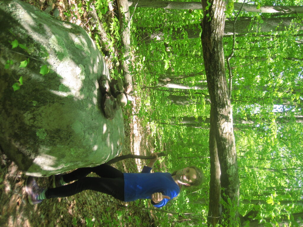 K making a thumbs up sign in front of a downed tree, a turning in the path and a cairn